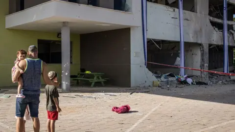 A father shows his children a heavily-damaged school in Israel's southern city of Gedera on October 2, 2024, after Iran launched a barrage of missiles at Israel