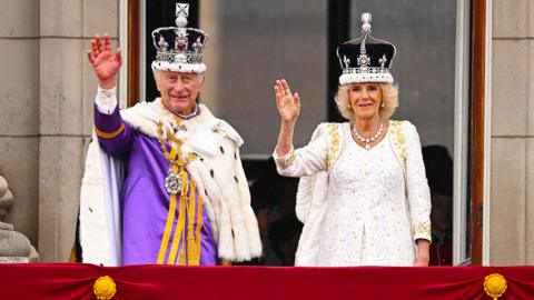 King Charles and Queen Camilla on the Buckingham Palace balcony wearing crowns and robes