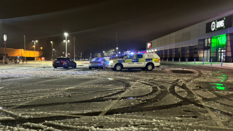 A police car with other cars in a car park in Spytty, Newport, with skid marks visible in the snow in front