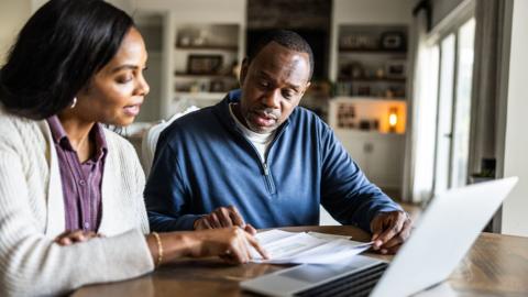 Husband and wife looking over bills and using laptop in domestic kitchen - stock photo