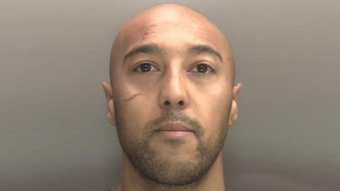 Police mugshot of Cameron Hancel. He has a clean-shaven head, stubble on his face and a scar-like marking under his right eye