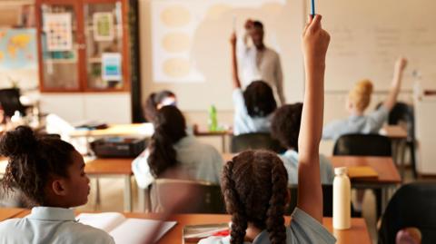 A scene of children raising their hands in a classroom