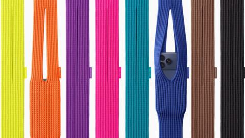 A display of eight brightly coloured knitted iPhone Pocket bags, two with iPhones in them, coloured from the left yellow, orange, purple, pink, turquoise, blue, brown and black. 