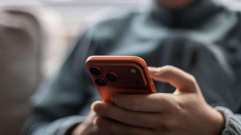 A young person in a grey tracksuit jacket holds a red iPhone.