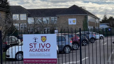 Large brick-built school building with railings in front and "St Ivo Academy" sign