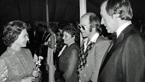 Pop star Sir Elton John and television personality David Frost meeting Queen Elizabeth II in 1977