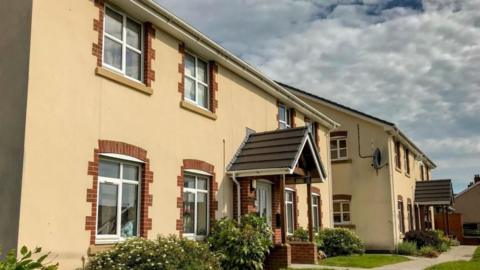 A view of some social housing in Pontypridd, with yellow walls, white framed windows and a porch in view.