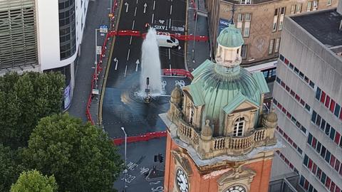 An aerial view  of a large jet of water gushing from the middle of a road