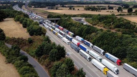 Hundreds of lorries on a motorway. They are queueing heading out of the frame.