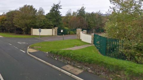 The exterior of Heron and Brearley a road, with walls and a gate leading to the entrance of the site. 