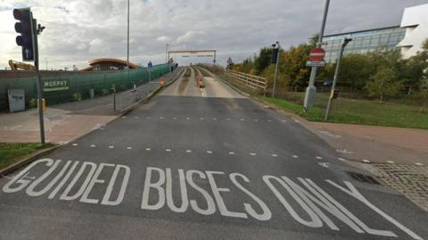 A road leading to a bridge. Written on the tarmac ahead of the bridge in white letters it says guided buses only. 