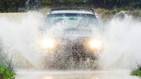 A car drives through rain and puddles