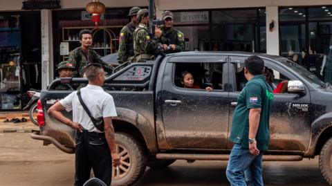 Armed men on the back of a vehicle as passersby look on