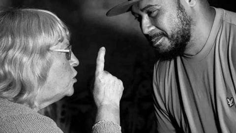 An elderly woman wagging her finger at a young man