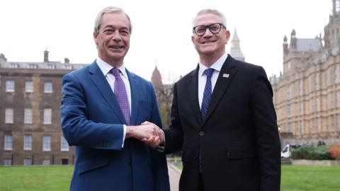 Two men in suits shake hands on College Green in Westminster