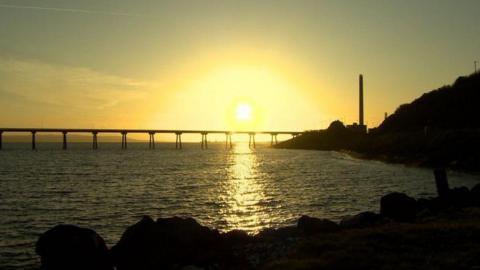 The sun is setting over the Irish sea. The chimney from the site can be seen in the background. 