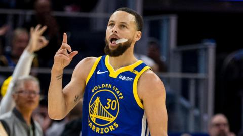 Stephen Curry pictured holding up his finger with a gumshield hanging out of his mouth