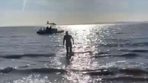 Harrison in the water, the sun is shining on the water and there is a boat behind him