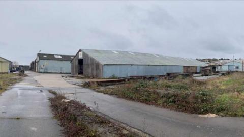 Two large grey timber yards set in a commercial area, with concrete hardstanding leading to their entrance.