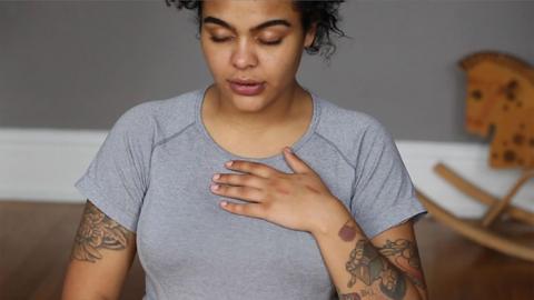 A tattooed woman breathes with her hand on her chest.