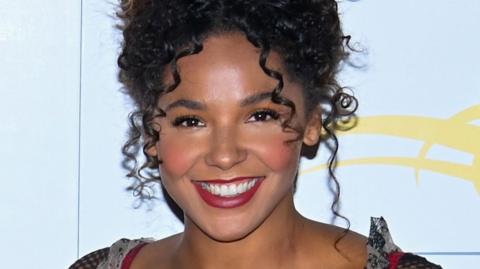 A smiling woman with curly hair is smiling brightly