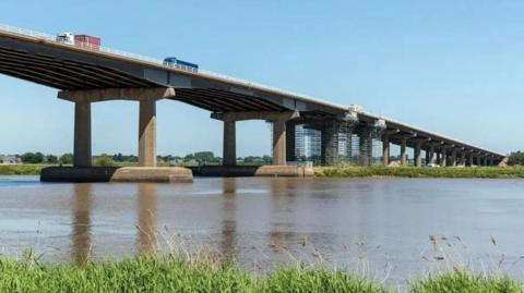 A large concrete motorway bridge carrying cars and lorries spans the River Ouse near Goole, scaffolding can be seen on the side of the bridge.