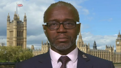 Insp Tola Munro from Avon and Somerset Police faces the camera. He is in his police uniform and the Houses of Parliament are in the background