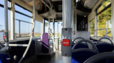 A close up of a stop button inside an empty bus with seats in mixture of fabrics and colours