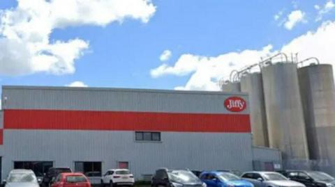 A Jiffy factory in grey and red with cars parked at the front