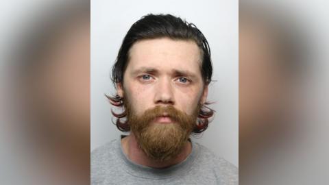 A police mugshot of Joshua Rothery, who has long dark hair and a ginger beard.