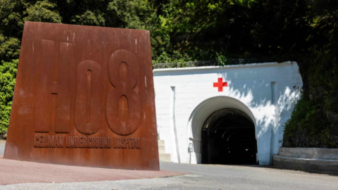 The entrance to Jersey War Tunnels, there is a large metal sign saying 'german underground hospital' and a white tunnel behind it.