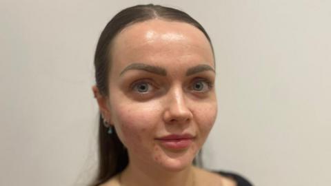 A woman with straight brown hair looks straight at the camera 