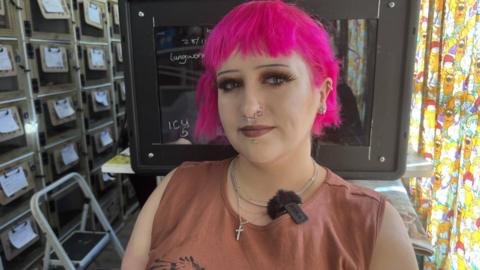 Savannah wearing a dark orange top with pink hair, stood in the middle of the hedgehog rescue centre