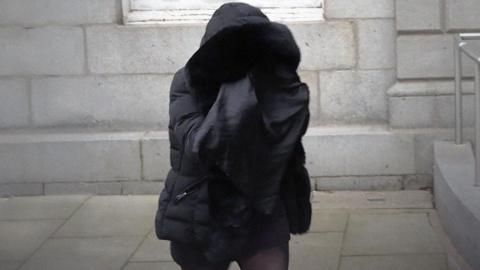 A person wearing a parka walks outside a court building covering her face in a black material