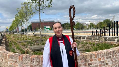 The Bishop of Hull standing near the burial site. She is dressed in robes and is holding a crozier in her left hand.