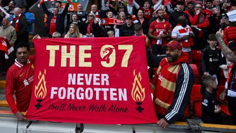 A crowd of Liverpool Football Club supporters holding a banner which reads 'The 97 never forgotten, you'll never walk alone', on the anniversary of the disaster in 2025 at Hillsborough stadium