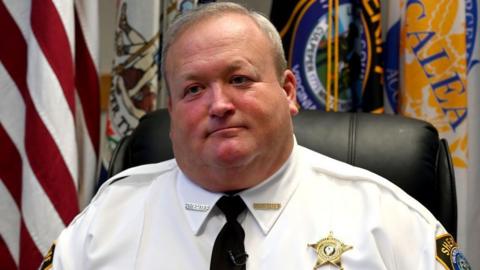 Former Culpeper County Sheriff Scott Jenkins wearing a white shirt, black tie with a gold badge on the right side