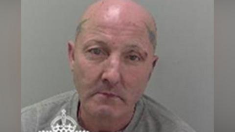 Julian Thomas in a police mugshot. He has a bald head and tattoos on both sides of his head. He is wearing a grey sweatshirt.