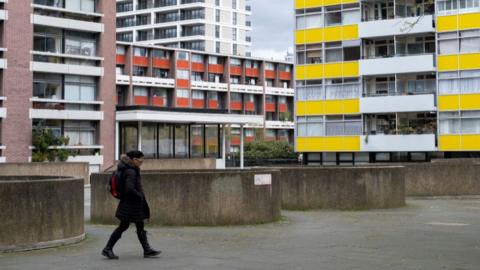 An image of a woman wearing a black coat walking past a housing estate in London
