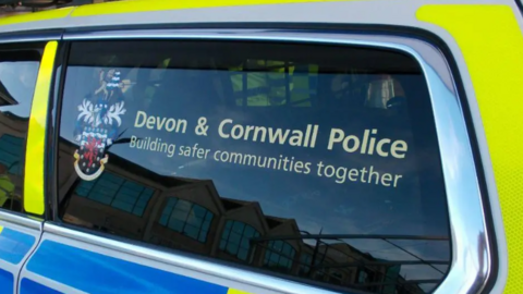 A Devon and Cornwall Police vehicle. A window has a Devon and Cornwall Police sticker. The car is neon blue and yellow. 