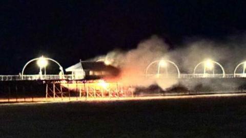 Smoke and fire billows from Southport Pier surrounded by black sky.