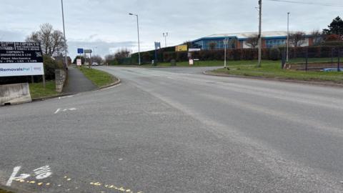 A wide road featuring road markings and lamposts in the background.