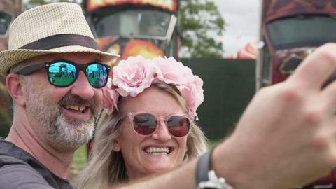 A man and a woman taking a selfie in front of some colourful vehicles