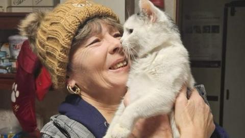 A volunteer holds a cat and smiles lovingly at it