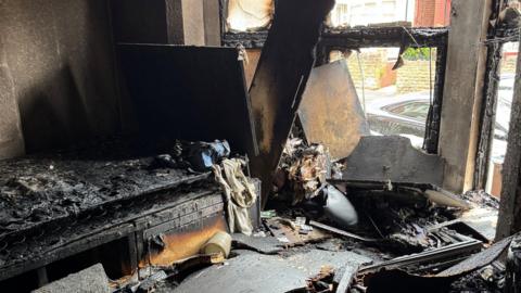 The room badly damaged by fire. The window is smashed through and the furniture is severely burned 
