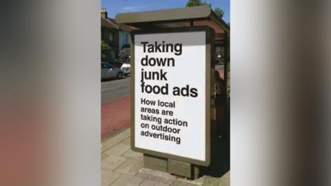 An advert on a bus stop reads 'taking down junk food ads'