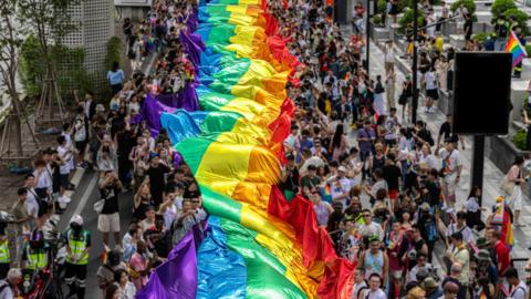 Group of People Celebrating Gay Pride Parade- Pride Month and Parade-People marching with the rainbow LGBTQ+ flag - stock photo
