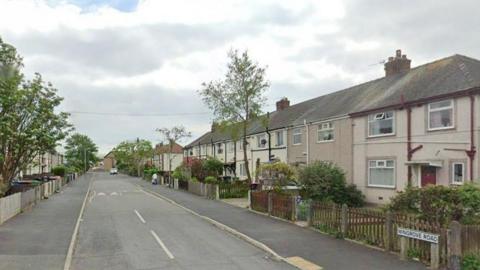 A row of terraced houses are on each side of a road, with a sign saying 'Wingrove Road'.