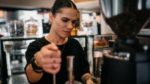 Female barista wearing a black T-shirt operating a coffee machine