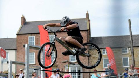 A stunt rider jumping his bike in the air while a crowd watches the show.